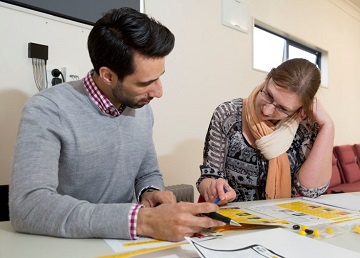 Two people working together at a table, reviewing documents and taking notes.