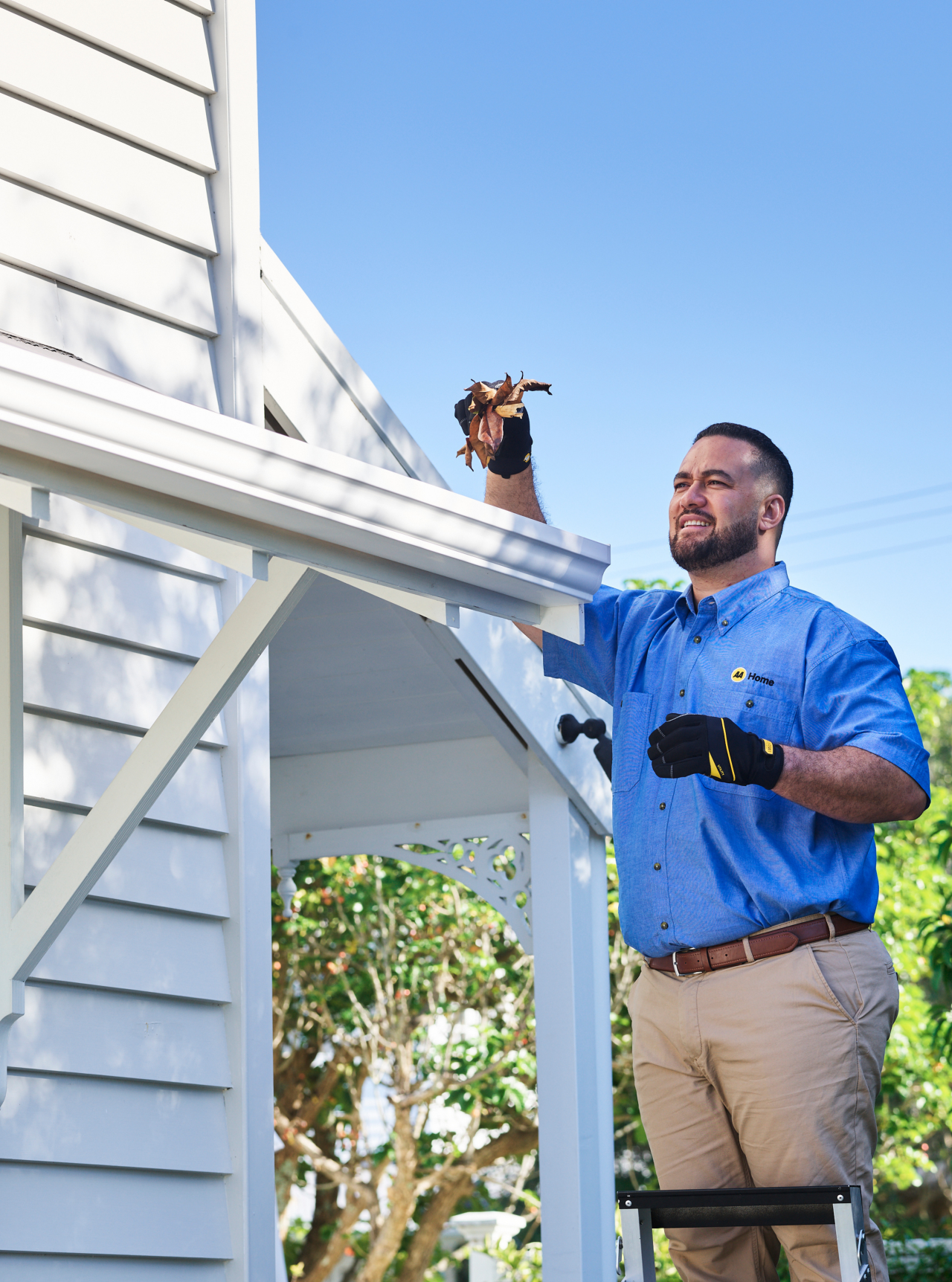 AA Home tradesman on a ladder cleaning the roof gutter 
