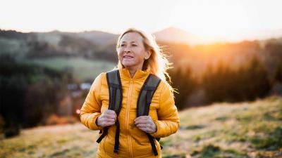 Older woman on a hillside with the sun setting behind her