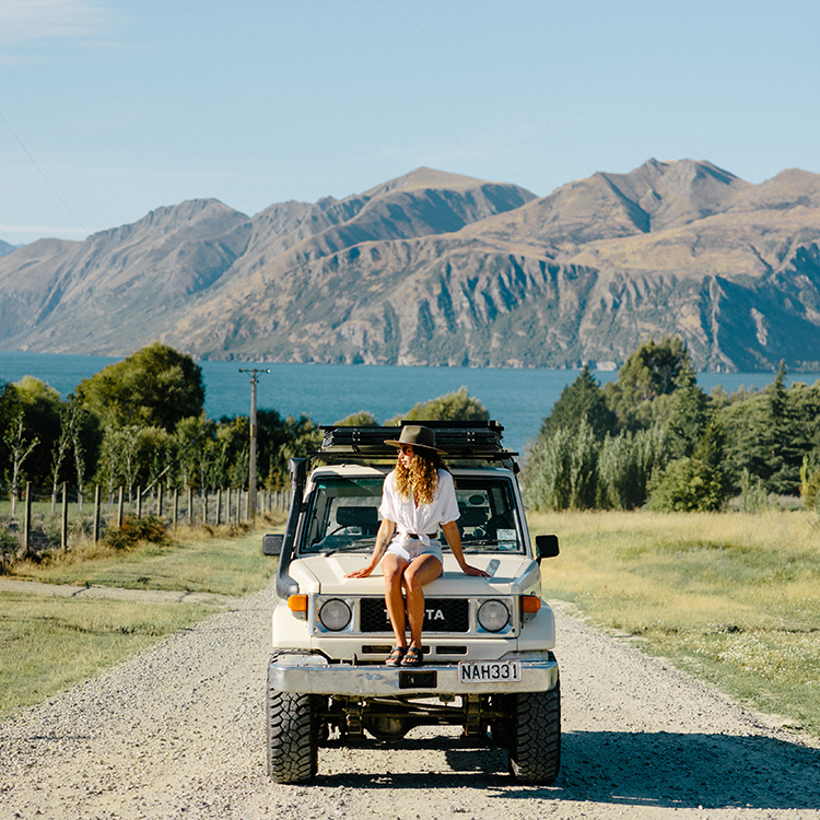 Woman sitting on the front of her truck with the water in the background