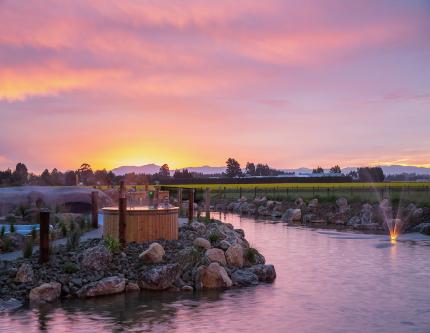 Two people soak in a hot tub at sunset at Ōpuke Thermal Pools, Methven