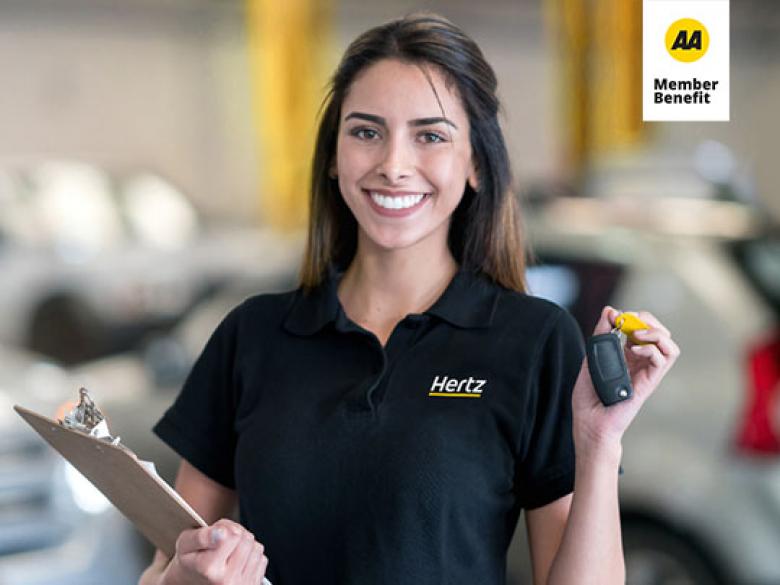 Young woman in a Hertz staff polo holding up car keys in one hand and a clipboard with the other.