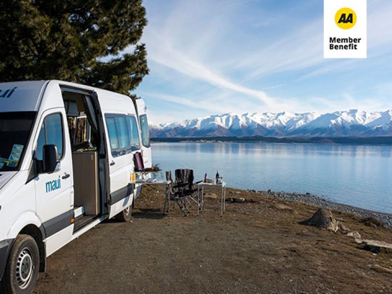 Parked Maui campervan next to a lake and mountain range.
